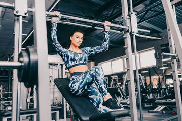 Young woman with ponytail at the gym using fitness equipment. Satisfied girl relax and enjoying her training. She is relaxing hanging upon the bar. Close up. View from the right side