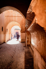 Narrow red alley street in medina of Marrakech, Morocco. Silhouette of a man in traditional jellaba going through archways of old town on a sunny day. 
