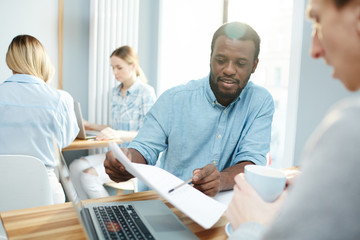 Attractive African-American man demonstrating documents for Caucasian guy while working in office together