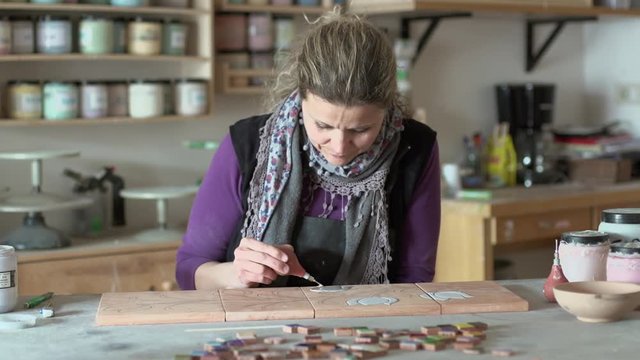 Medium shot of woman ceramist working on tiles with technique of cuerda seca