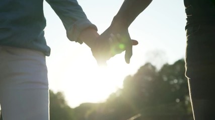 In this close up slow motion footage you can see young couple holding hands in evening sunset backlit.