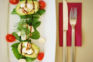 Avocado salad with mozzarella cheese, cherry tomatoes, herbs and sauce in a plate on the table in a restaurant.
