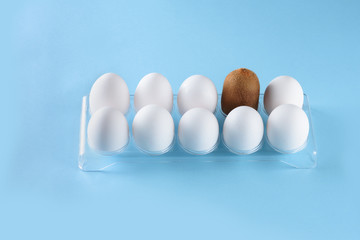 Kiwi standing out from crowd of plenty identical white eggs in plastic box background. Leadership, uniqueness, independence, new idea, initiative, strategy, dissent, think different, business success