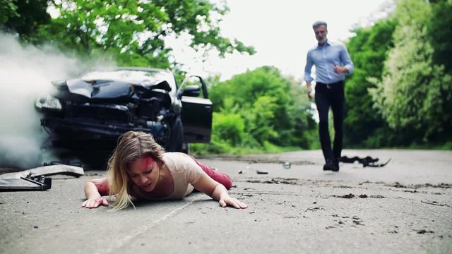 A man running towards a young woman lying on the road after a car accident.