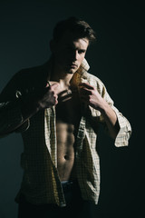 Man with torso, muscular macho with six packs, dressing shirt, dark background. Guy looks confident and attractive. Macho on pensive face, muscular figure, sportsman, bodybuilder. Masculine concept.