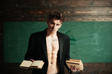 Teacher on pensive face, muscular figure, holds books in hand. Sexy teacher concept. Man with muscular torso, six packs, wears classic jacket and eyeglasses, looks attractive, chalkboard on background