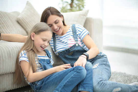 Mother with a little daughter using a smartphone sitting in the new living room