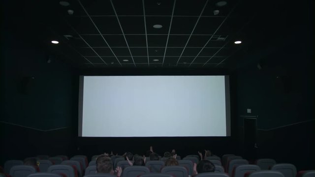 Spectators sitting in front of white screen in cinema. Spectator looking on cinema white screen. People applauding in front of cinema screen in movie theatre