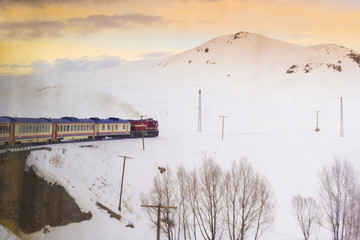 Red passenger diesel train moving on historical bridge. Snow covered railway tracks - East express between Ankara and Kars - Turkey