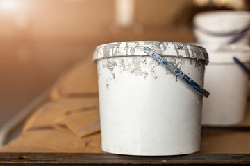 Close-up used white dirty plastic paint bucket in room. Renovation and repair process concept....