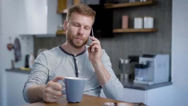 A man is sitting in his kitchen, and talking on the phone. Breakfast, coffee and a pleasant time for conversation with friends.