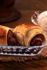 Baked sausages in puff pastry with a golden  crust in a glass plate on a linen cloth napkin on a wooden background.