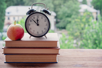 an alarm clock and an apple on a pile of books on the windowsill