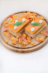 Two pieces of delicious cake on wooden board decorated with floral petals