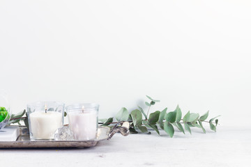 White room interior decor with burning candle and greenery, copy space on white wall