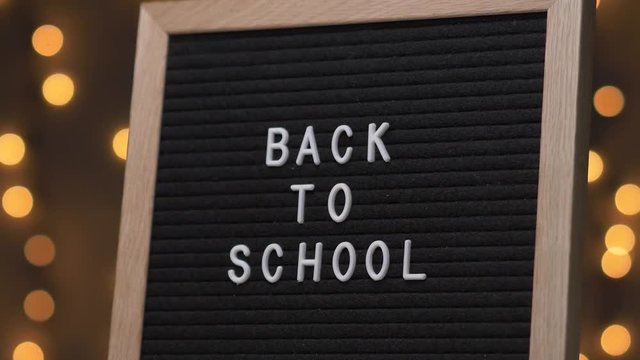 Black letter board with BACK TO SCHOOL Written on it with white letters. Camera rotating around the sign showing the beautiful bokeh balls in the background.