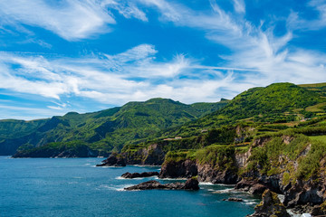 The coast line of Flores island in Azores, green landscape with blue sky and some Clouds