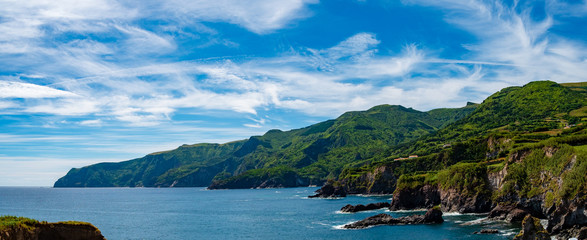 The coast line of Flores island in Azores, green landscape with blue sky and some Clouds