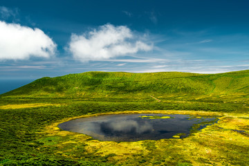 A blue lagoon in Flores island Azores, with a green mountain and a blue sky with some clouds
