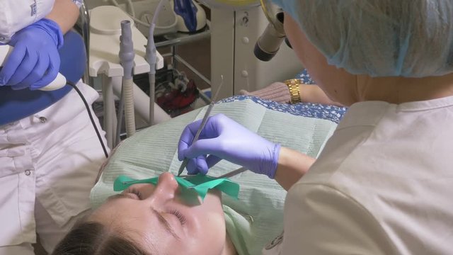 Woman at dentist clinic gets dental treatment to fill a cavity in a tooth. Dental restoration and composite material polymerization with UV light and laser. The doctor works with an assistant.