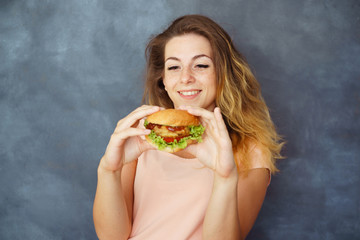 Fast-food, diet, self-control, appetite, satisfaction, delight, unhealthy eating. Young cute woman with hamburger in hands enjoying food