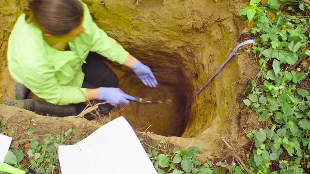 Woman scientist environmentalist sitting in a soil slit, taking samples of a soil and putting them into the paper envelope