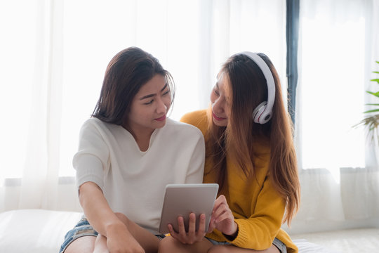 Two asia woman enjoy listening music app on tablet sitting on sofa in living room at home.Leisure digital lifestyle.Lesbian lgbt couple. - Powered by Adobe