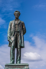 Fototapeta na wymiar Edinburgh, Scotland, UK - June 13, 2012: Just the Abraham Lincoln bronze statue on Old Calton Cemetery isolated against blue cloudy sky.