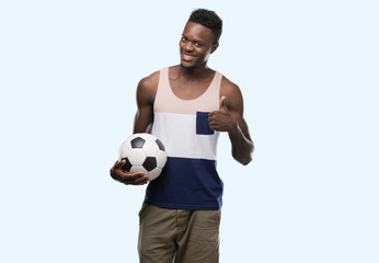 Young african american man holding soccer football ball happy with big smile doing ok sign, thumb up with fingers, excellent sign