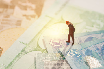 Europe economy, financial, investment or currency exchange concept, miniature businessman figurine standing and looking at Euro sign on pile of banknotes - obrazy, fototapety, plakaty