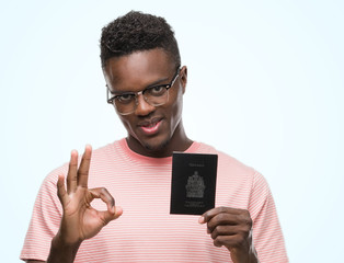 Young african american man holding canadian passport doing ok sign with fingers, excellent symbol