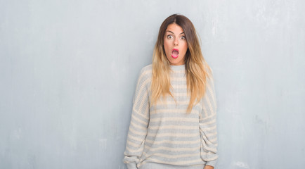 Fototapeta premium Young adult woman over grunge grey wall wearing winter sweater afraid and shocked with surprise expression, fear and excited face.