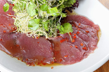 Fish Carpaccio with olives ana salad. Served on a white plate.