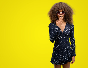 African american woman with sunglasses and summer dress cover mouth with hand shocked with shame for mistake, expression of fear, scared in silence, secret concept