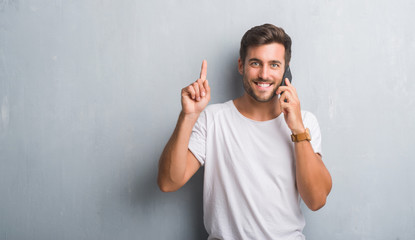 Fototapeta premium Handsome young man over grey grunge wall speaking on the phone surprised with an idea or question pointing finger with happy face, number one