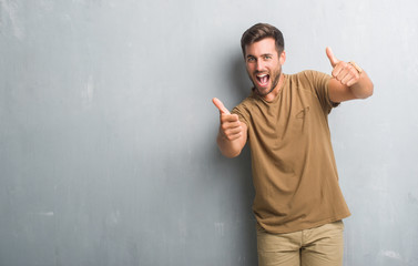 Handsome young man over grey grunge wall approving doing positive gesture with hand, thumbs up...
