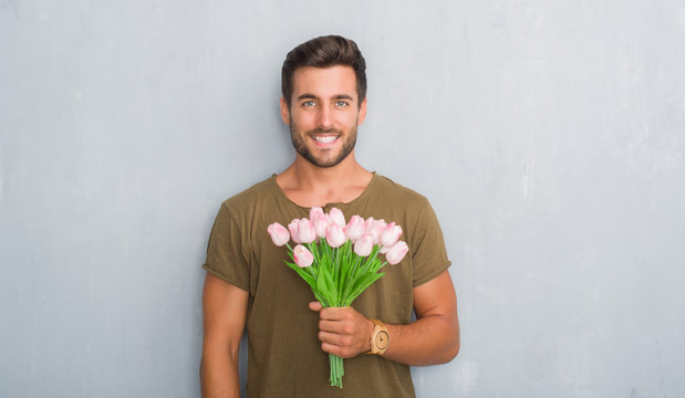 Handsome Young Man Over Grey Grunge Wall Holding Flowers Bouquet With A Happy Face Standing And Smiling With A Confident Smile Showing Teeth