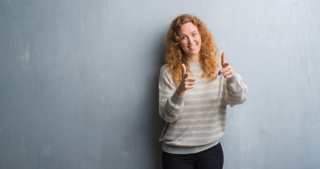 Fototapeta premium Young redhead woman over grey grunge wall pointing fingers to camera with happy and funny face. Good energy and vibes.