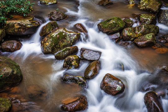 Long exposure scene of flowing water with white wave through rock river from waterfall in tropical rainforest.