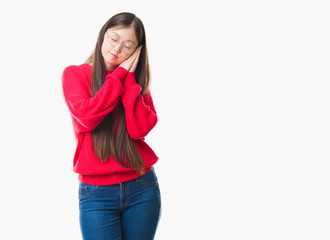 Young Chinese woman over isolated background wearing glasses sleeping tired dreaming and posing with hands together while smiling with closed eyes.