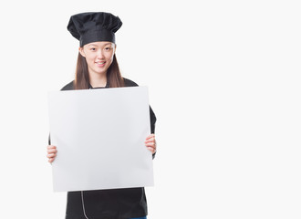 Young Chinese woman over isolated background wearing chef uniform holding banner with a happy face standing and smiling with a confident smile showing teeth