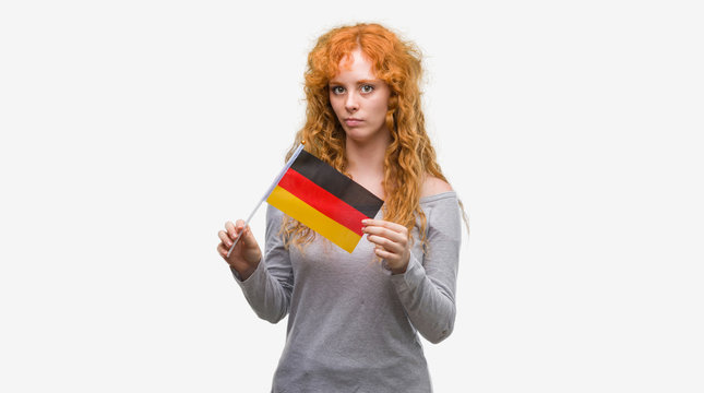 Young redhead woman holding flag of Germany with a confident expression on smart face thinking serious