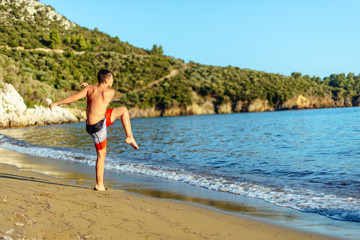 Boy on sand shoots the ball into the blue sea