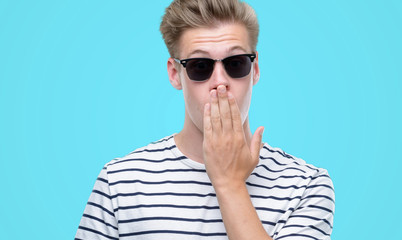 Fototapeta premium Young handsome blond man wearing sunglasess cover mouth with hand shocked with shame for mistake, expression of fear, scared in silence, secret concept