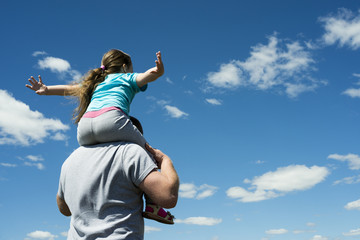 Obraz premium father and daughter playing outdoors, against the blue sky. Cheerful child, happy family, father's day.