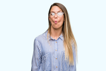 Beautiful young woman wearing elegant shirt and glasses making fish face with lips, crazy and comical gesture. Funny expression.