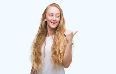 Blonde teenager woman pointing and showing with thumb up to the side with happy face smiling
