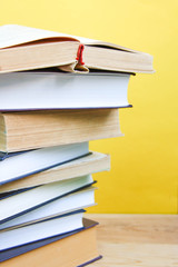 Back to school and knowledge concept. Stack of books on wooden background and trendy yellow wall