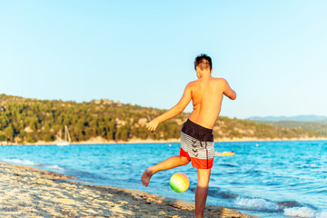 Alone boy playing football at the beach