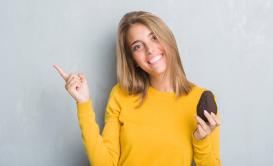 Beautiful young woman over grunge grey wall eating avocado very happy pointing with hand and finger to the side